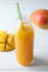 Tasty mango juice in glass bottle and fresh fruits on white wooden table, closeup