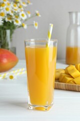 Tasty mango juice in glass, fresh fruits and chamomile flowers on white wooden table, closeup
