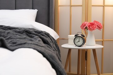 Side table with alarm clock and decor near bed indoors