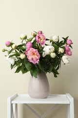 Bouquet of beautiful peony flowers in vase on shelving unit against beige background