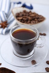 Cup of aromatic coffee, beans and star anise on white table, closeup