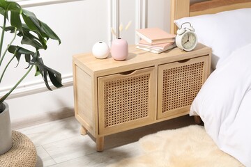 Bedside table with alarm clock, books and decor near bed indoors © New Africa