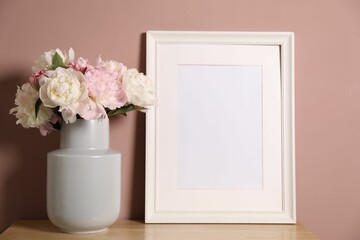 Beautiful peonies in vase and picture frame on wooden dresser near pink wall. Space for text