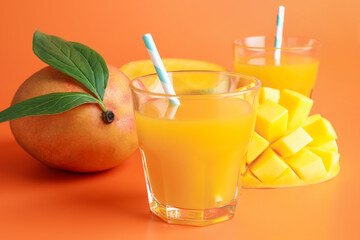 Tasty mango juice in glasses and fresh fruits on orange background, closeup