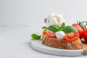 Tasty sandwich with mozzarella cheese, tomatoes and basil on light tiled table, closeup. Space for...
