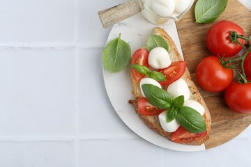 Tasty sandwich with mozzarella cheese, tomatoes and basil on light tiled table, top view. Space for text