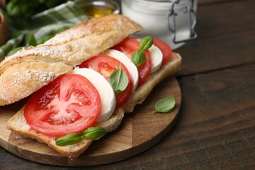 Tasty sandwich with mozzarella cheese, tomatoes and basil on wooden table, closeup