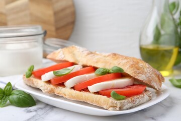Tasty sandwich with mozzarella cheese, tomatoes and basil on white marble table, closeup