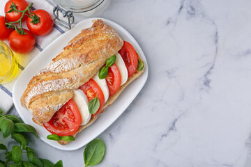 Tasty sandwich with mozzarella cheese, tomatoes and basil on white marble table, flat lay. Space for text