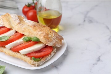 Tasty sandwich with mozzarella cheese, tomatoes and basil on white marble table, closeup. Space for text