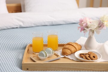 Tray with delicious breakfast and flowers on bed indoors, closeup. Space for text
