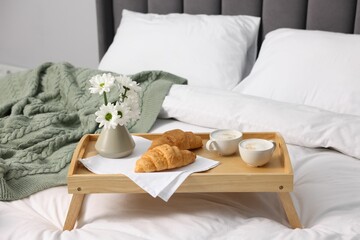 Tray with delicious breakfast and flowers on bed indoors, closeup. Space for text