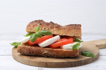 Tasty sandwich with mozzarella cheese, tomatoes and basil on white wooden table, closeup