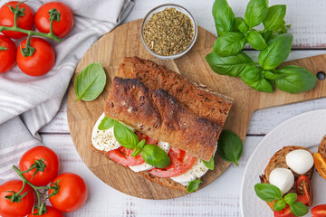 Tasty sandwich with mozzarella cheese, tomatoes and basil on white wooden table, flat lay