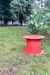 Bright red cable spool in a lush park with green foliage, ideal for industrial outdoor,...