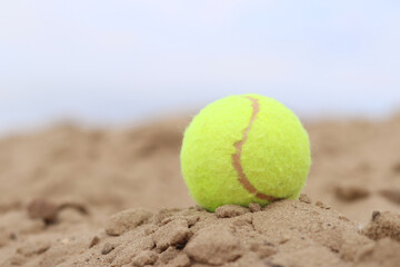 Yellow tennis ball lies on the sand. Sports and recreation concept, summer games. Tennis or paddleball ball. Tennis court near the beach. Paddleball ball on the sand near the water. Outdoor games