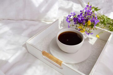 A bouquet of wild flowers and coffee on a tray in the bedroom on the bed in the morning.
