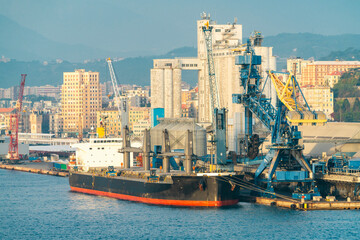 Bulk carrier at industrial port with cranes and city skyline, Savona