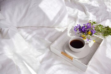 A bouquet of wild flowers and coffee on a tray in the bedroom on the bed in the morning.