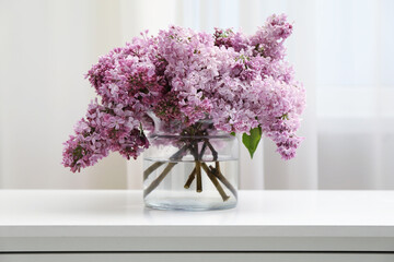 Beautiful lilac flowers in glass vase on white table indoors