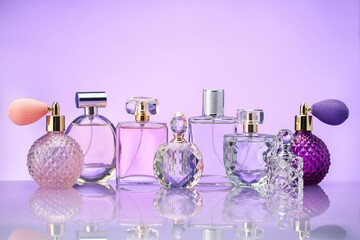 Bottles of perfume on mirror surface against violet background