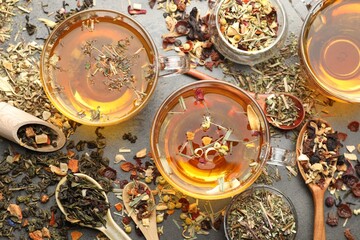 Aromatic herbal tea and dry leaves on grey table, flat lay