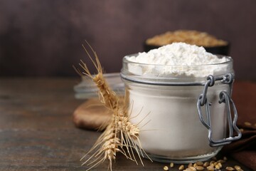 Wheat flour, grain and spikes on wooden table, closeup. Space for text