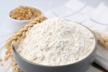 Wheat flour, grain and spikes on white table, closeup