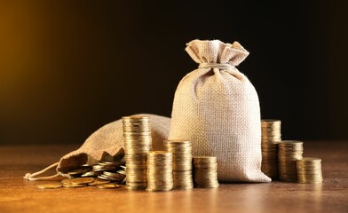 Bags and stacked coins on wooden table against dark yellow gradient background © New Africa