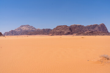 Wadi Rum Desert Horizon: The vast expanse of Wadi Rum desert stretches out under a clear blue sky,...