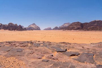 Naklejka premium Wadi Rum Desert Landscape: A panoramic view of the Wadi Rum desert in Jordan, showcasing vast expanse of red sand, rugged mountains, and clear blue sky.