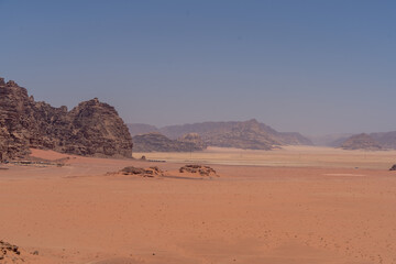 Camels walking through a sandy desert landscape with mountains under a clear sky