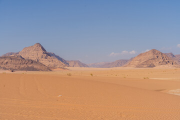 Desert Landscape Under Azure Skies: A sweeping panorama of an arid desert stretches towards a distant mountain range, where endless horizons meet the clear blue sky in this captivating scene