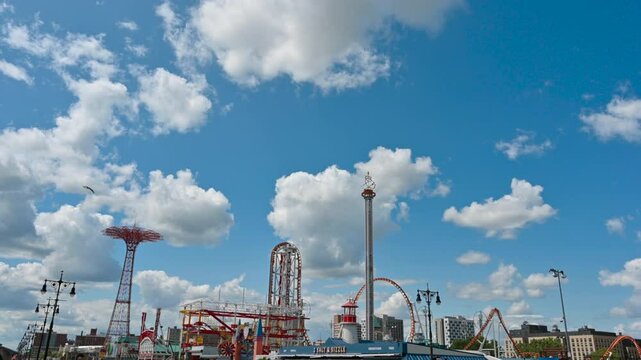 New York City, USA, August 21, 2024. Wide angle panoramic view of coney island amusement park. Beautiful summer day, white clouds slowly moving across the blue sky.