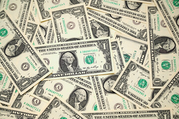 Numerous one-dollar bills are arranged haphazardly on a flat surface