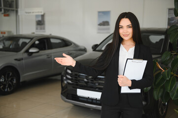 Saleswoman showing new car in dealership holding clipboard