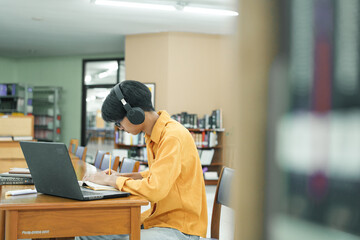 Young collage student using computer and mobile device studying online in library.