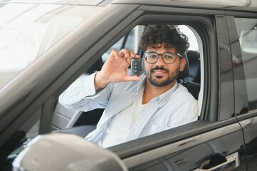 Happy man showing car key sitting in new vehicle in dealership