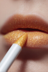 Golden lipstick is being applied to shimmering lips. Beauty and glamour
