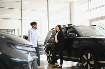 Saleswoman showing new car to customer in dealership