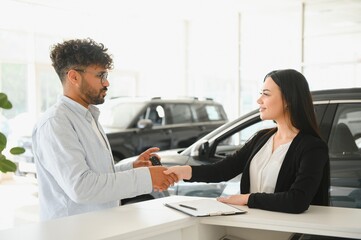 Fototapeta premium Saleswoman shaking hands with customer buying new car in dealership