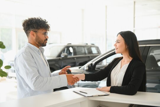Saleswoman shaking hands with customer buying new car in dealership