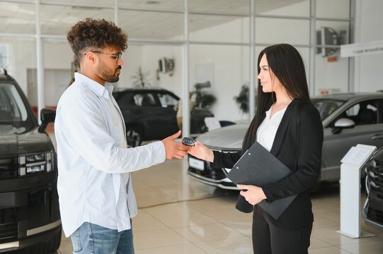 Saleswoman giving car keys to customer in dealership - Powered by Adobe