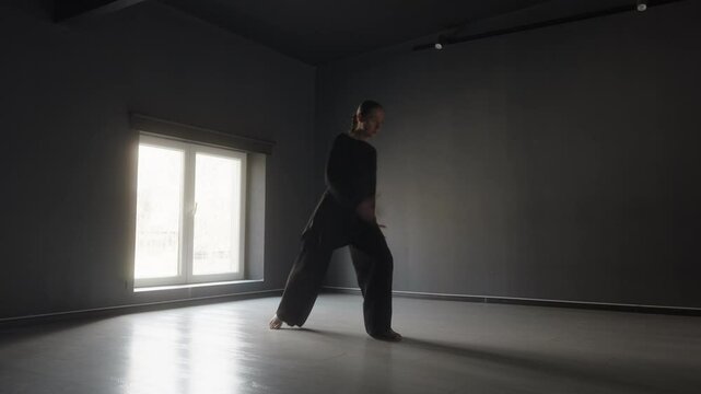 A woman in black performs an interpretive dance in a dark studio.