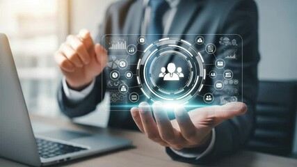 Man in suit holding a digital interface with team icon and laptop in blurred background view close up - Powered by Adobe