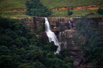 Dramatic Dainthlen waterfall cascades down a rocky cliff amidst lush green foliage.