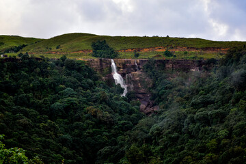 Dramatic Dainthlen waterfall cascades down a rocky cliff amidst lush green foliage.