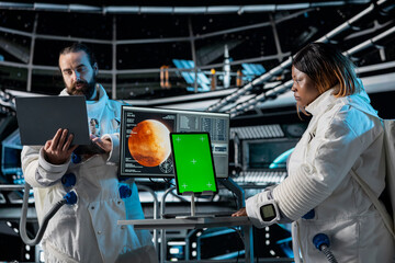 Orbital station coworkers analyzing Mars planetary data using green screen tablet. Team of...