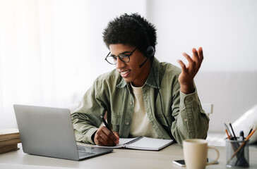 Online communication and web based learning. Positive black teenager speaking to his college tutor on laptop from home. Handsome African American student making video call on webcam