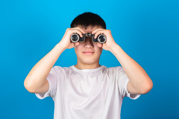 Young Asian boy using binoculars against blue background